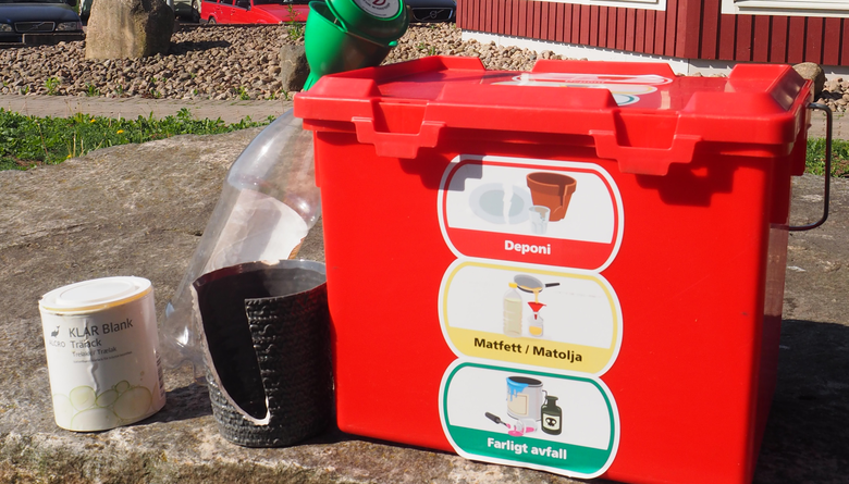 Röd miljöbox med målarfärgsburk, kruka samt plastflaska med oljekort bredvid. 